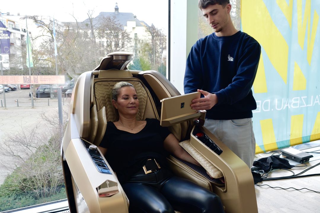 Een klant zit achterovergeleund in een massagestoel, een medewerker laat haar de instellingen op het scherm zien